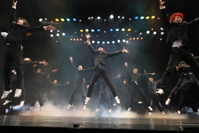 コンドルズの公演写真。黒い詰襟学生服を着たたくさんのダンサーが大の字になってジャンプしている写真。